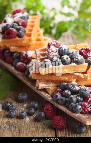 Leckere süße Waffeln mit Himbeeren und Blaubeeren auf einem alten Holztisch. Stockfoto