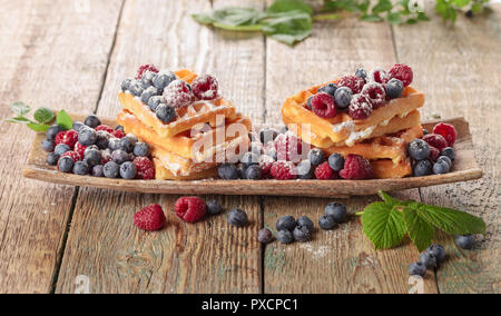 Leckere süße Waffeln mit Himbeeren und Blaubeeren auf einem alten Holztisch. Stockfoto