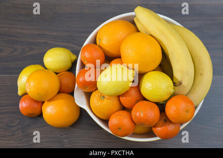 Überblick über eine Obstschale mit Zitrusfrüchten und Bananen, Orangen, Zitronen, Mandarinen, neben einer kleinen Gruppe von mehreren Zitrusfrüchte auf dem gr Stockfoto