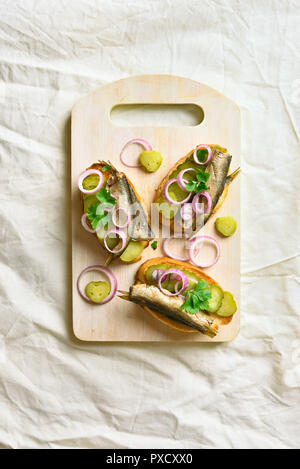 Sandwiches mit Sprotten, marinierten Gurken und Zwiebeln auf Holzbrett. Ansicht von oben, flach Stockfoto