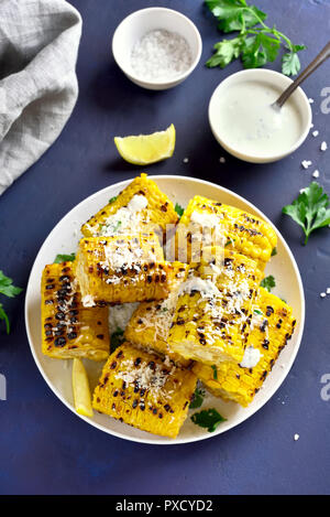 Gebratene Maiskolben mit Soße und Parmesan über blauen Stein Hintergrund. Ansicht von oben Stockfoto