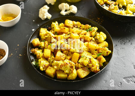 Lecker Aloo Gobi indische Gericht. Gebratener Blumenkohl mit Kartoffeln auf schwarzen Steintisch. Stockfoto