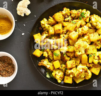 Nahaufnahme von Aloo Gobi indische Gericht. Gebratener Blumenkohl mit Kartoffeln auf schwarzen Stein Hintergrund. Ansicht von oben Stockfoto