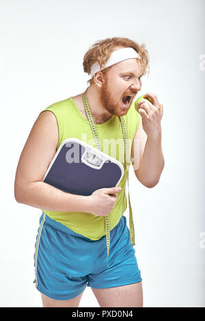 Lustiges Bild von roten Haaren, bärtigen, dicker Mann auf weißem Hintergrund. Mann mit einem Apfel und Skalen Stockfoto