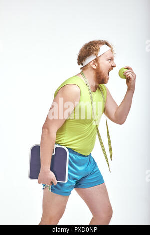 Lustiges Bild von roten Haaren, bärtigen, dicker Mann auf weißem Hintergrund. Mann mit einem Apfel und Skalen Stockfoto