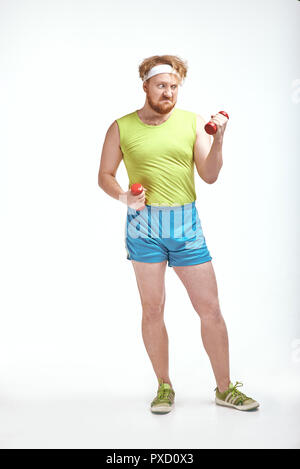 Lustiges Bild von roten Haaren, bärtigen, dicker Mann auf weißem Hintergrund. Mann Sportkleidung zu tragen. Mann hält die Hanteln Stockfoto