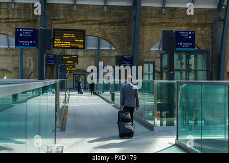 Ein Geschäftsmann mit Koffer Spaziergänge entlang der Brücke zwischen Plattformen am Bahnhof King's Cross, London, UK Stockfoto