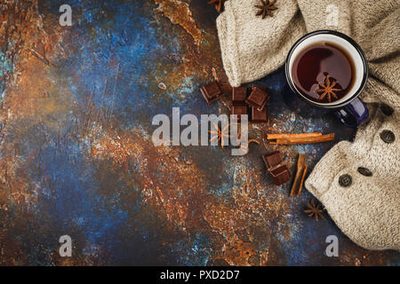 Blau emailliert Tasse Tee, Zimtstangen, Anis Sterne, dunkle Schokolade und warmen Wollpullover auf einem dunklen Hintergrund. Ansicht von oben. Platz für Text. Stockfoto