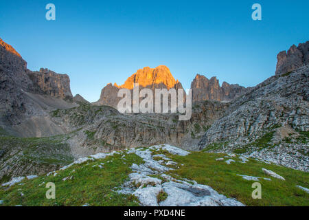 Erste Tageslicht in den Bergen, leuchtende Berg Wand in den Sonnenaufgang. Gras, Steine und Felsbrocken. Wolkenlosen blauen Himmel. Stockfoto