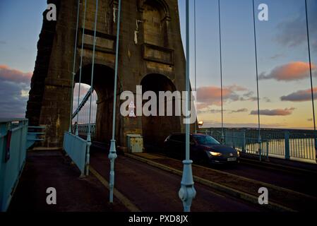 Ein Auto überquert die Menai Suspension Bridge in der Morgendämmerung, Bangor, Wales, Großbritannien Stockfoto