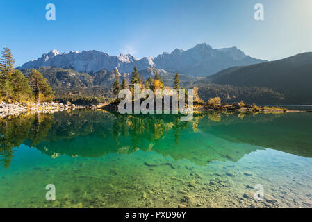 Herbst farbige Bäume auf dem Braxeninsel im Eibsee vor dem Gipfel der Zugspitze im Wettersteingebirge, Deutschland Stockfoto