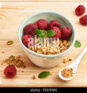 Hausgemachtes Müsli in der Schüssel mit Himbeeren auf hölzernen Tisch. Stockfoto