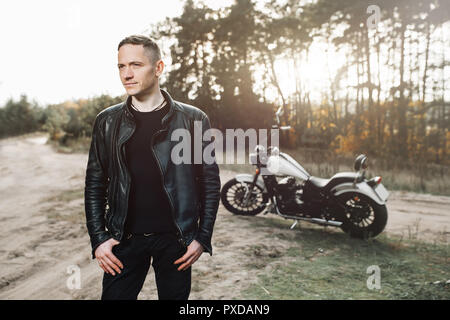 Stattliche rider Kerl in schwarzer Biker Lederjacke auf klassische Art Café Racer Motorrad bei Sonnenuntergang. Bike custom in vintage Garage gemacht. Brutale Spaß urba Stockfoto