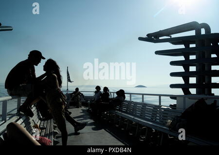 Griechenland, eine kleine Inselfähre, fährt über die Ägäis. Urlauber können die Sommersonne auf der Dachterrasse genießen. Die Menschen beginnen ihren Urlaub. Stockfoto