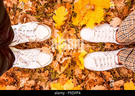 Blick von oben auf die männliche und weibliche Füße in weißem Leder Sneakers stehen einander gegenüber auf gelb und orange Blätter im Herbst im Park Stockfoto