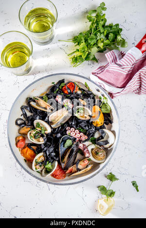 Hausgemachte Meeresfrüchte schwarzer Pasta Spaghetti mit Venusmuscheln vongole Muscheln Octopus in der Wanne mit Weißwein auf Marmoriertem Hintergrund Stockfoto