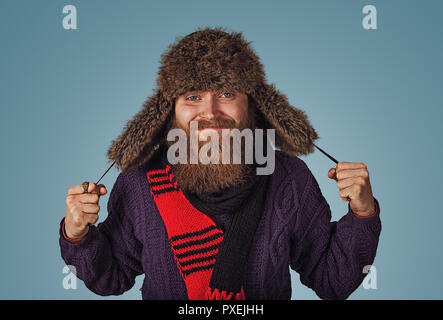 Bärtiger Mann Holding mit flauschigen Fell hat in roten Schal lila Pullover auf Blau studio Wand Hintergrund isoliert. Positive Gesichtsausdruck menschliche Emotion Stockfoto