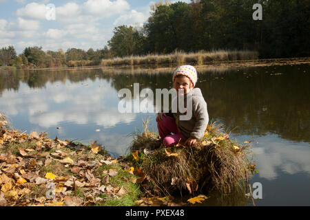 Little cute boy/girld vor POSING am See, in einem bunten Wetter im Herbst. Wetter: Sonnig, weiße Wolke, bunten Natur. Stockfoto