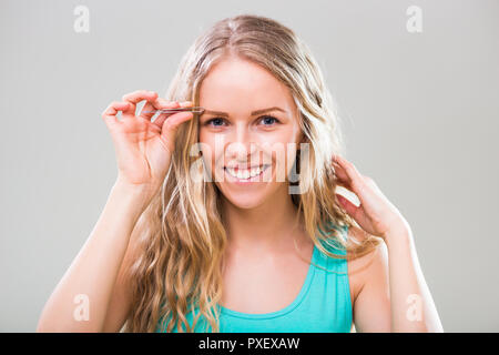 Schöne junge Frau Zupfen der Augenbrauen auf grauem Hintergrund. Stockfoto