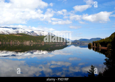 Den verschneiten Rocky Mountains in British Columbia, Kanada, im Frühling, mit einem Spiegel See spiegelt die hellen blauen und weißen Himmel und Wolken Stockfoto