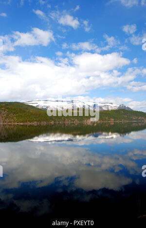 Den verschneiten Rocky Mountains in British Columbia, Kanada, im Frühling, mit einem Spiegel See spiegelt die hellen blauen und weißen Himmel und Wolken Stockfoto