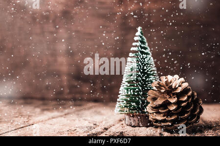 Weihnachtsbaum und Gold Pine Cone und Schnee auf grunge Holz Tisch und dunkelbraunen Holz Wand. Winter frohe weihnachten urlaub Grußkarte Stockfoto