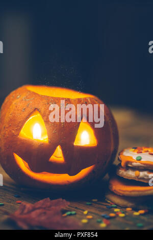 Halloween Hintergrund mit Kürbis auf dem Holztisch. Lächeln Pumpkin Head mit Kerzen, Herbstlaub und Halloween Cookies. Nahaufnahme Stockfoto