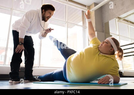 Übergewichtige junge Frau arbeitet mit Trainer Stockfoto