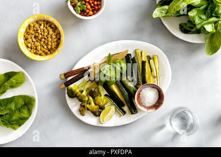 Gesundes Essen gebackenes Gemüse Zucchini mit Brokkoli, Spinat, Linsen und Kichererbsen auf konkreten Hintergrund der Ansicht von oben. Gesunde vegetarische Kost Stockfoto