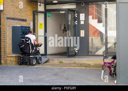Mann in einem elektrischen Rollstuhl, einem Metall Rampe in einem Gebäude, Großbritannien Stockfoto