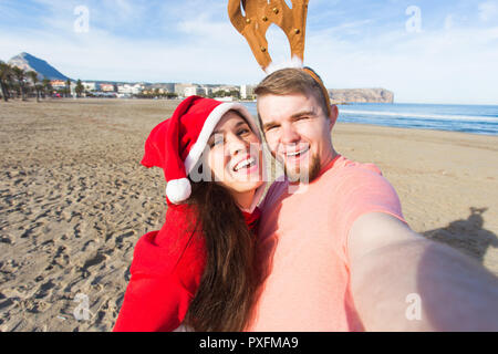 Spaß und Winterurlaub Konzept - glückliches Paar in Weihnachten Kostüme unter selfie über Sandstrand Hintergrund Stockfoto