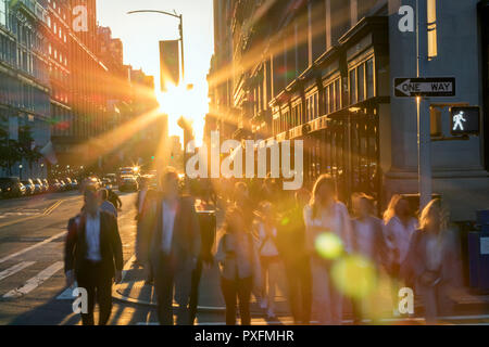 Masse des unscharfen Menschen Überqueren einer verkehrsreichen Kreuzung auf der 5th Avenue in New York City mit dem hellen Licht des Sonnenuntergangs im Hintergrund Stockfoto