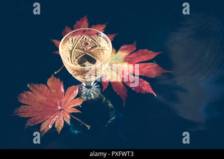 Herbst Hintergrund mit Wein in Kristallglas auf dem Hintergrund der roten Ahornblätter. Stockfoto