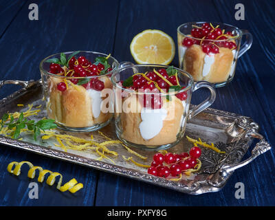 Drei Glas Tassen Limoncello (oder limoncino) Tiramisu gekrönt mit rote Johannisbeeren und Minze, auf einem silbernen Tablett auf einem dunklen Hintergrund Stockfoto