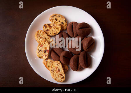Cookies in Form von Kaffeebohnen und Müsli mit Rosinen und Nüssen auf einem weißen Teller. Stockfoto