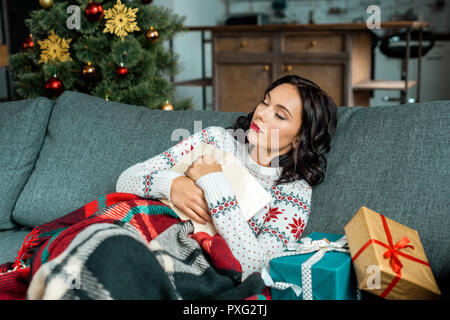 Schöne junge Frau mit Buch schlafend auf dem Sofa unter der Decke mit Geschenken in der Nähe von Weihnachten zu Hause Stockfoto