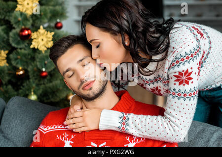 Selektiver Fokus der attraktiven Frau küssen schlafen Freund auf dem Sofa in der Nähe von Weihnachten zu Hause Stockfoto