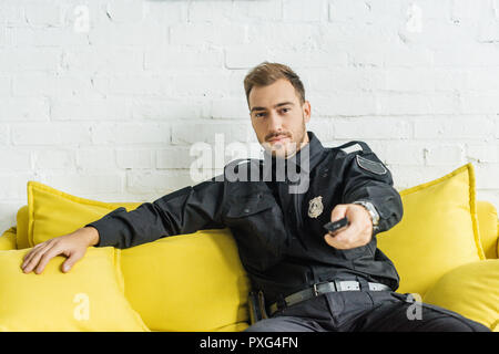 Hübscher junger Polizist sitzen auf der Couch und mit Hilfe der TV-Fernbedienung Stockfoto