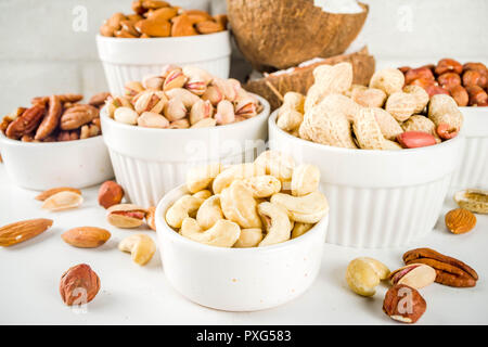 Verschiedene Arten von Nüssen - Walnüsse, Pekannüsse, Erdnüsse, Haselnüsse, Mandeln, Kokos, Cashews, in Schalen, auf einem weißen Marmor Tabelle Ansicht von oben Stockfoto