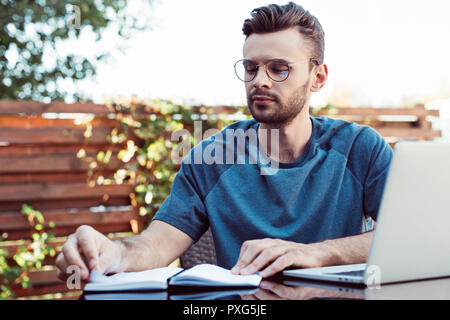 Nachdenklich, stattlicher Mann in Gläsern im Webinar und Notebook im Park Stockfoto