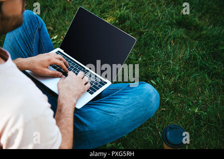 Zugeschnittenes Bild der Mann mit Laptop mit leerer Bildschirm im Park Stockfoto