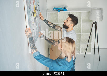 Seitenansicht des Jungen tätowierten Paar hängende Gemälde an der Wand in der neuen Wohnung Stockfoto