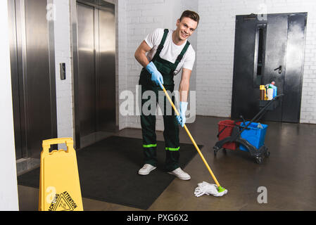 Hübscher junger Hausmeister wischen, und lächelnd an Kamera Stockfoto