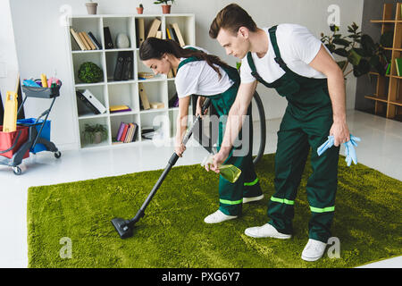 Junge Reinigung Firma Arbeitnehmer Reinigung Teppich mit Staubsauger und Reinigungsmittel einsprühen Stockfoto