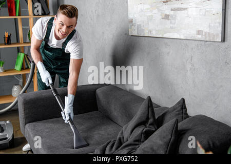 Hübscher junger Mann in Gummihandschuhe Reinigung Möbel und lächelnd an Kamera Stockfoto