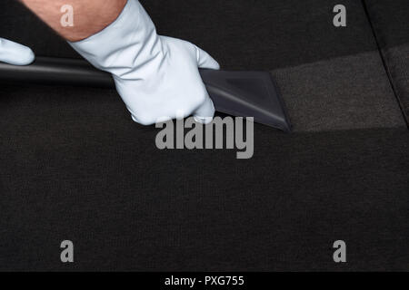 Close-up Teilweise mit Blick auf die Person in Gummihandschuhe Sofa mit Staubsauger reinigen Stockfoto