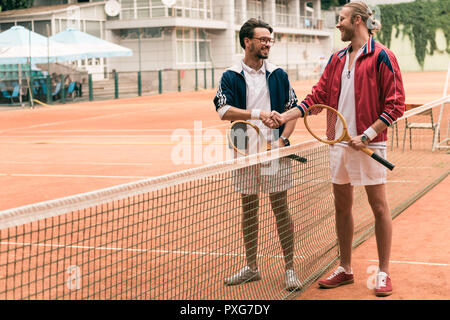 Freunde mit hölzernen Schläger Hände schütteln auf Tennisplatz mit Net Stockfoto