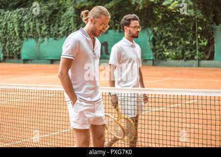 Tennis Spieler in Weiß Sportswear mit hölzernen Schläger zu Fuß in der Nähe von Netto auf Gericht Stockfoto