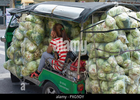 Ein markt anbieter Blätter Pak Klong Talad, ein Ganzes - Verkauf Gemüse-, Obst- und Blumenmarkt in Bangkok, Thailand, ihr Tuk-Tuk mit Kohl überlastet Stockfoto