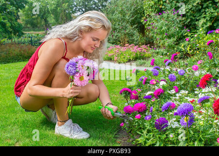 Junge holländische Frau Pflaumen bunte Sommerblumen im Hinterhof Stockfoto